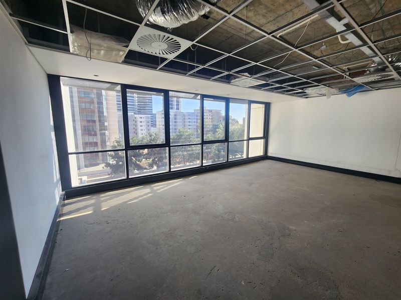 An unfinished office space featuring large windows with city views, exposed ceiling grid, and concrete flooring, ready for custom fit-out.
