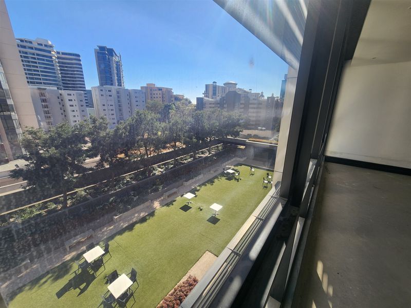 An elevated view from an office interior looking out over a landscaped courtyard with artificial turf and surrounding urban buildings.