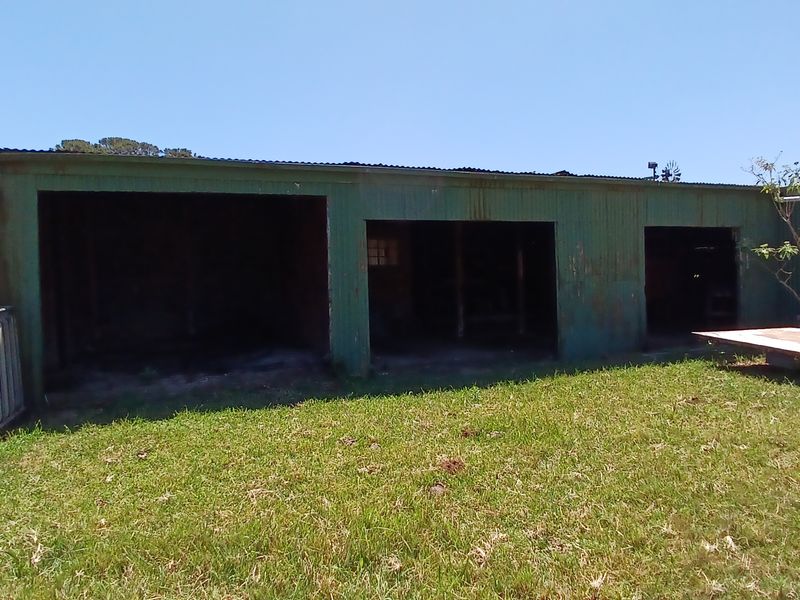 A multi-bay farm outbuilding or garage featuring corrugated metal construction, showing significant signs of weathering and surface corrosion.