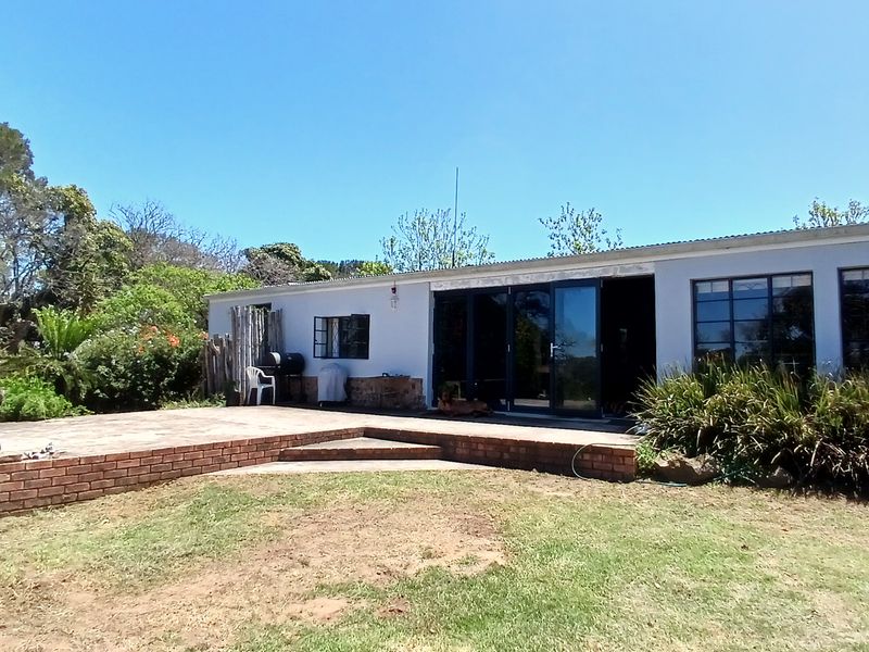 Rear view of the farm dwelling featuring a brick patio, large sliding glass doors, and metal-framed windows set against a landscaped garden.