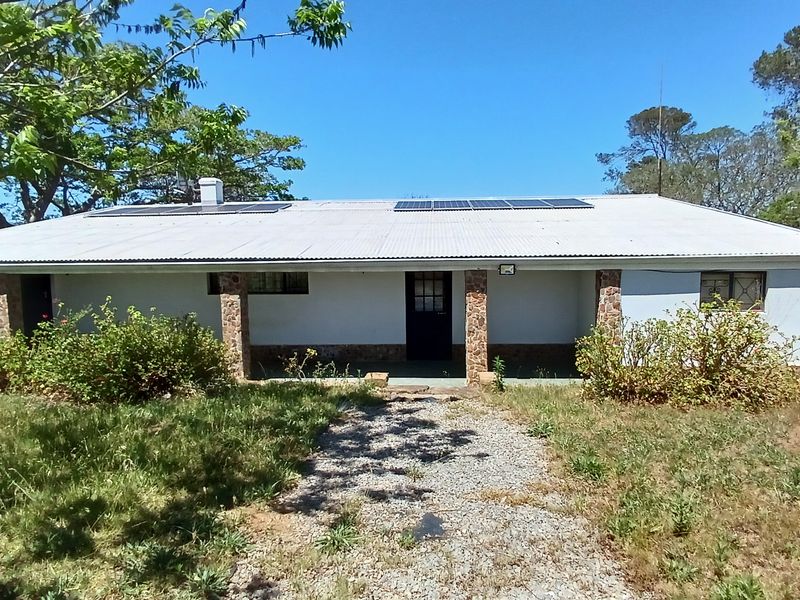 Front view of a single-story farm house featuring a corrugated metal roof with solar panels, stone-clad pillars, and a covered entrance porch.