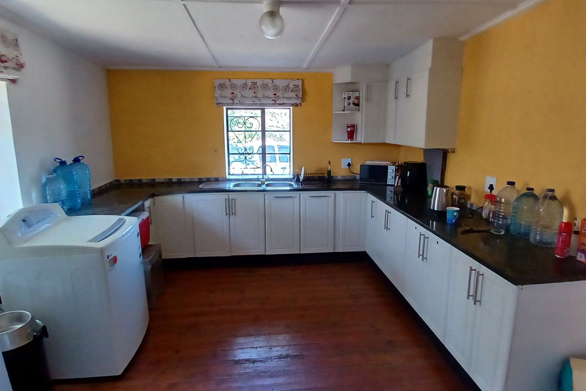 Functional kitchen featuring white built-in cabinetry, dark countertops, double basin sink, and timber flooring, offering a practical layout for daily use.