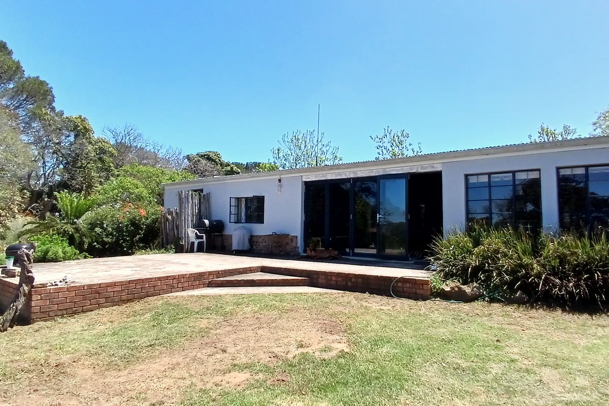 Rear view of the farm dwelling featuring a brick patio, large sliding glass doors, and metal-framed windows set against a landscaped garden.