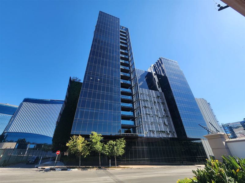 A modern high-rise office building featuring a striking glass curtain wall facade, integrated balconies, and a vertical garden element.