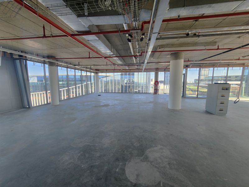 An open-plan office space in shell condition featuring floor-to-ceiling windows, exposed industrial ceilings, and concrete flooring, offering a blank canvas for custom fit-outs.
