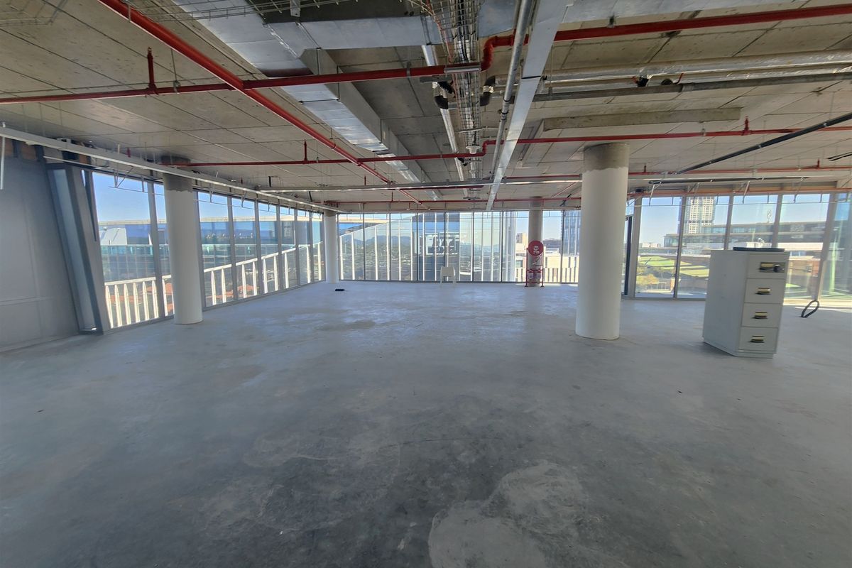 An open-plan office space in shell condition featuring floor-to-ceiling windows, exposed industrial ceilings, and concrete flooring, offering a blank canvas for custom fit-outs.