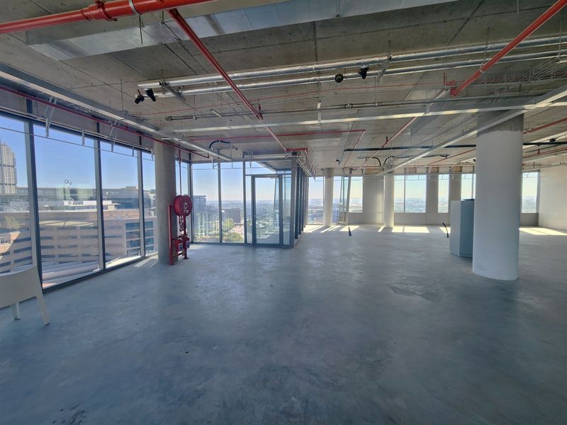 An expansive, open-plan office space in shell condition, featuring floor-to-ceiling windows, exposed industrial ceilings, and panoramic city views.