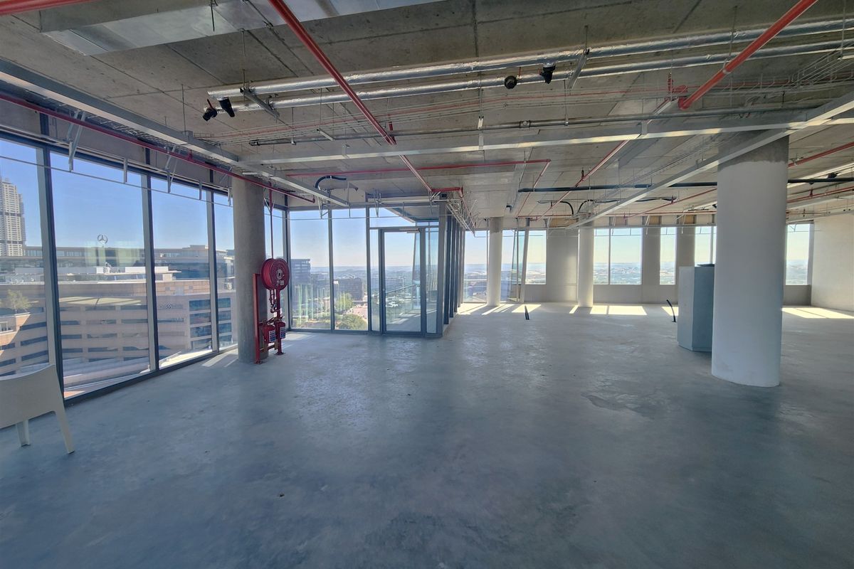 An expansive, open-plan office space in shell condition, featuring floor-to-ceiling windows, exposed industrial ceilings, and panoramic city views.