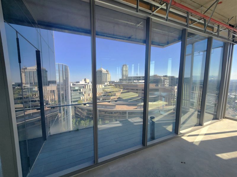 Unfinished office space featuring floor-to-ceiling windows, an attached balcony with glass balustrade, and expansive city views.