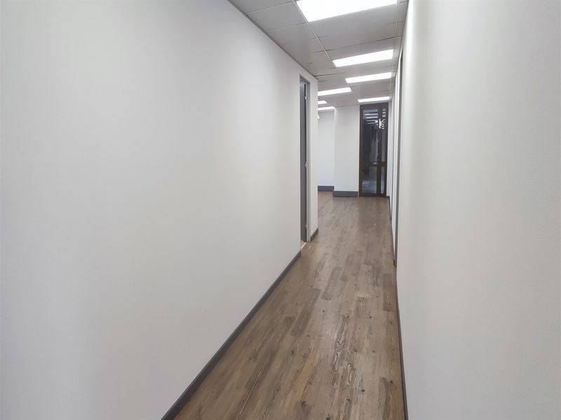A clean, modern office hallway featuring wood-look flooring, recessed ceiling lighting, and neutral walls, providing a professional and well-maintained circulation space.