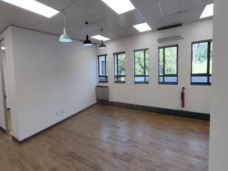 A bright, empty office space featuring laminate flooring, a suspended ceiling with integrated lighting, and a wall-mounted air conditioning unit.