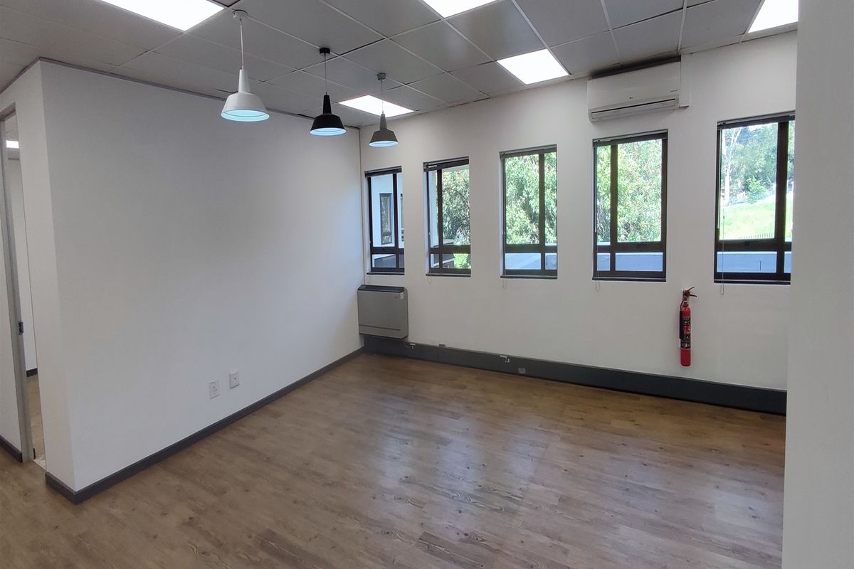 A bright, empty office space featuring laminate flooring, a suspended ceiling with integrated lighting, and a wall-mounted air conditioning unit.
