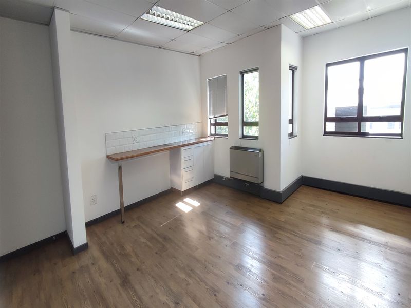 A bright, empty office space featuring laminate flooring, built-in cabinetry with a timber countertop, subway tile backsplash, and a wall-mounted air conditioning unit.