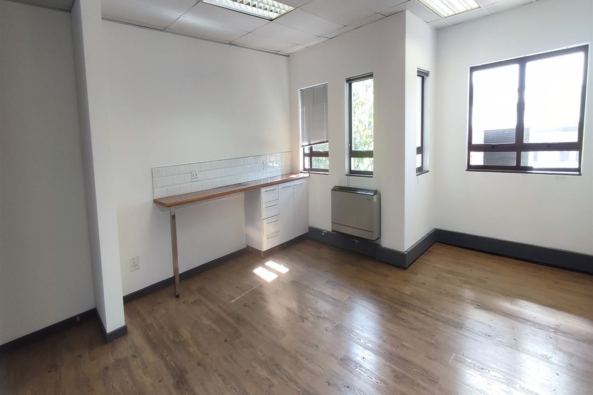 A bright, empty office space featuring laminate flooring, built-in cabinetry with a timber countertop, subway tile backsplash, and a wall-mounted air conditioning unit.