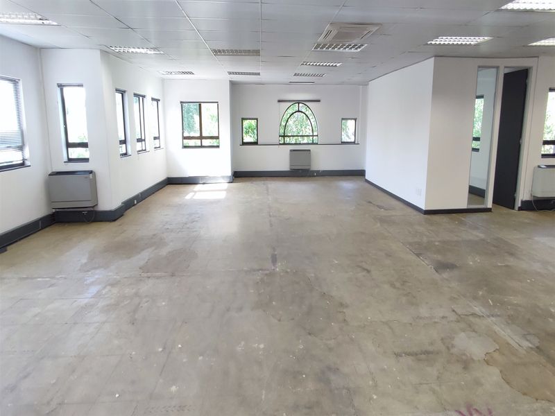 Spacious, empty office area featuring a suspended ceiling, recessed lighting, multiple windows, and air conditioning units, ready for custom flooring and fit-out.
