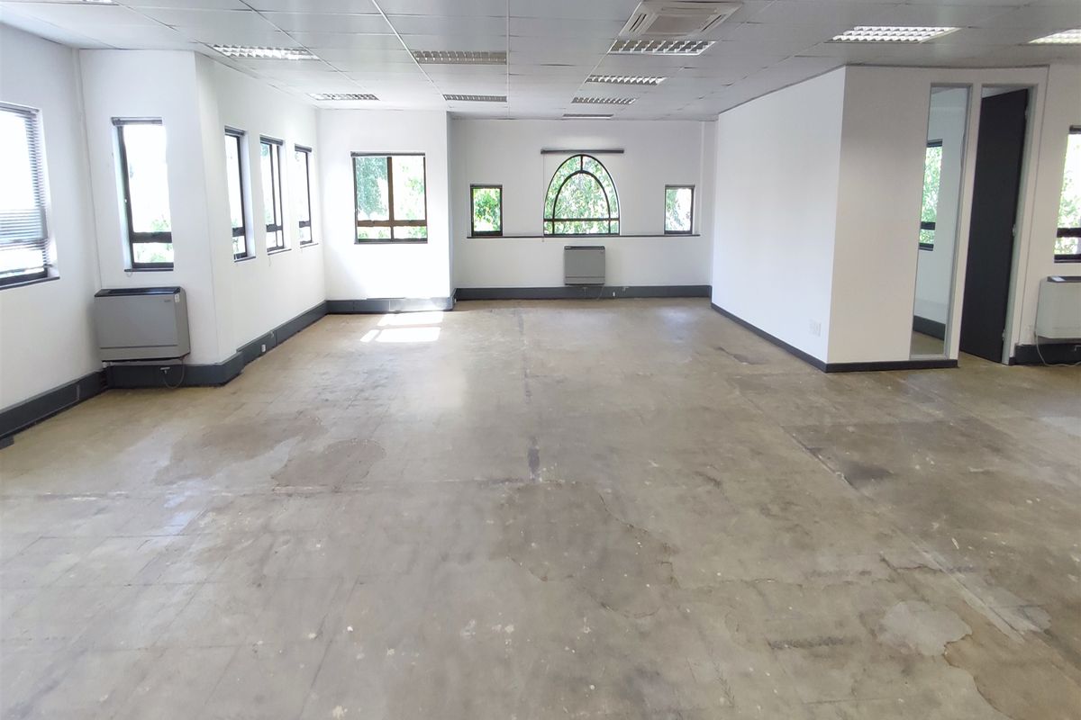 Spacious, empty office area featuring a suspended ceiling, recessed lighting, multiple windows, and air conditioning units, ready for custom flooring and fit-out.