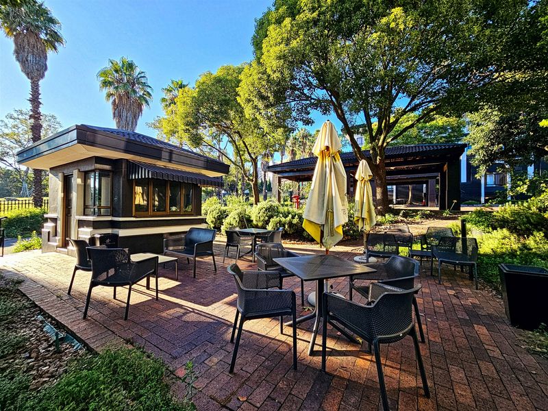 A well-maintained outdoor patio area featuring brick paving, surrounded by mature trees and landscaped garden space, ideal for office break-out or relaxation.