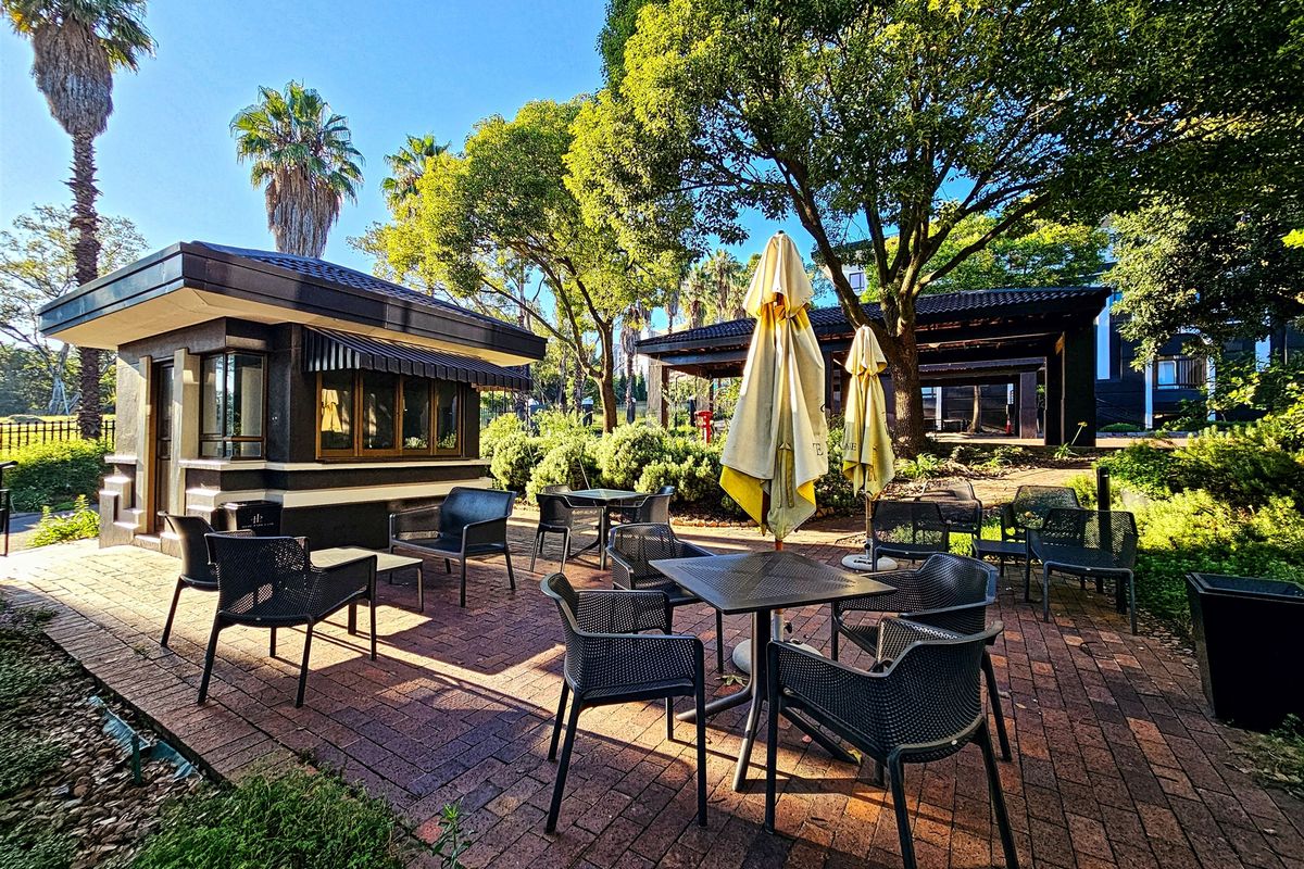 A well-maintained outdoor patio area featuring brick paving, surrounded by mature trees and landscaped garden space, ideal for office break-out or relaxation.
