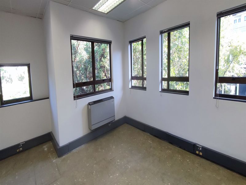 A vacant office space featuring large windows, wall-mounted HVAC unit, and practical skirting trunking for electrical connectivity.