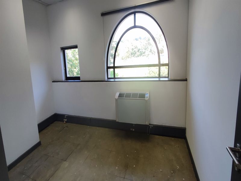 A vacant office space featuring an arched window, wall-mounted air conditioning unit, and tiled flooring, ready for refurbishment or custom fit-out.