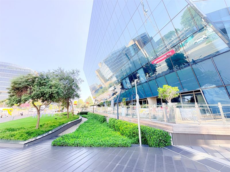 Modern office building exterior featuring a reflective glass facade, well-maintained landscaped gardens, and a paved pedestrian walkway.