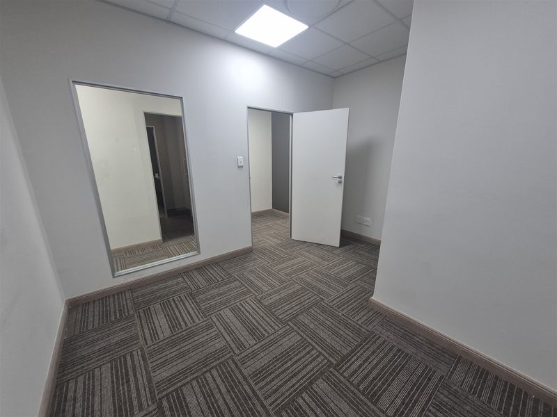 A clean, vacant office space featuring modern carpet tiles, a suspended ceiling with recessed lighting, and an internal glass partition.