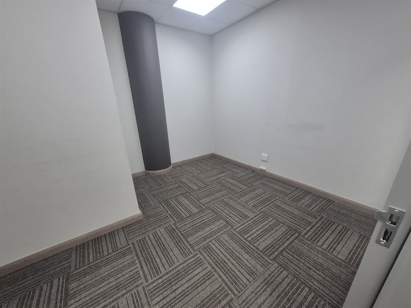 A clean, empty office space featuring modern carpet tiles, a structural column, and recessed ceiling lighting, ready for professional use.
