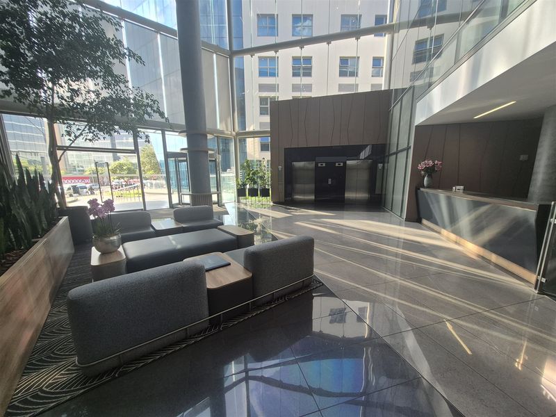 Modern office building lobby featuring a reception desk, floor-to-ceiling glass windows, and stainless steel elevator access.