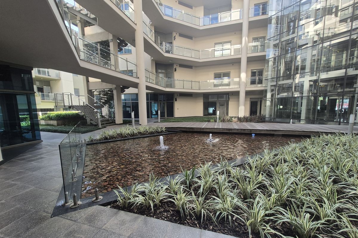 A modern office complex courtyard featuring a central water feature, timber decking, and multi-level glass-fronted office spaces with contemporary architectural finishes.