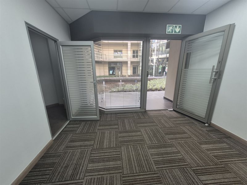 An empty office space featuring carpet tiles, a suspended ceiling, and glass doors providing direct access to an outdoor courtyard area.
