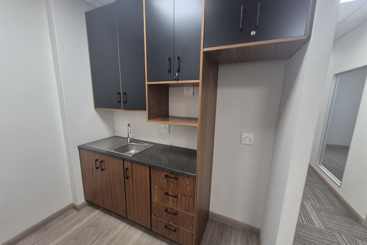 A clean, modern office kitchenette featuring two-tone cabinetry, a stainless steel sink, and durable laminate flooring.