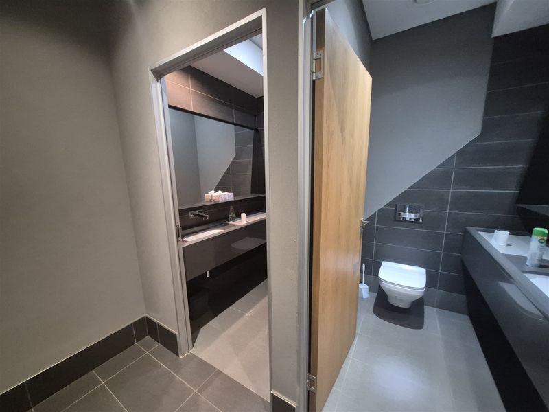 Modern office bathroom featuring high-quality dark grey tiling, wall-mounted toilet with concealed cistern, and a sleek built-in vanity area.