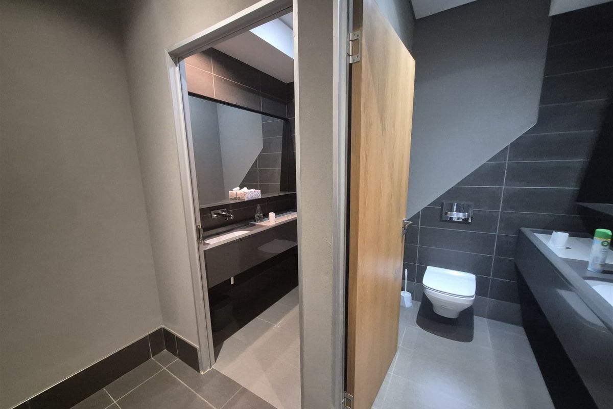 Modern office bathroom featuring high-quality dark grey tiling, wall-mounted toilet with concealed cistern, and a sleek built-in vanity area.