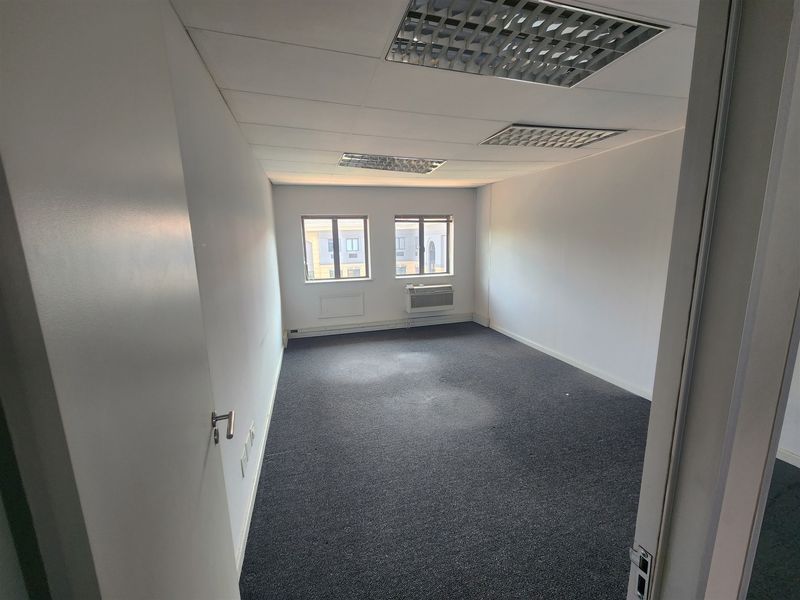 A vacant office space featuring neutral walls, carpeted flooring, recessed ceiling lighting, and a built-in window air conditioning unit.
