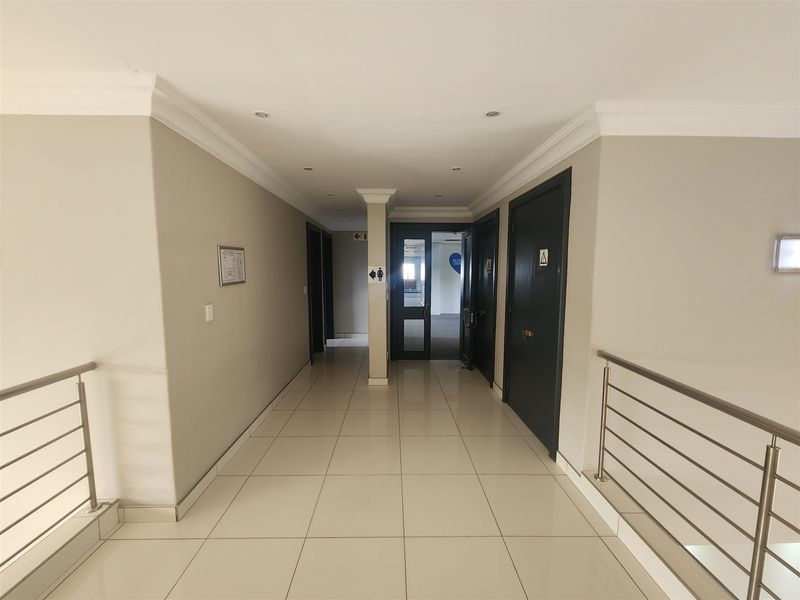 A clean, well-lit office hallway featuring tiled flooring, modern stainless steel balustrades, and professional solid core doors leading to various office suites.