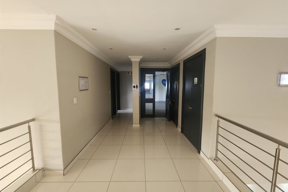A clean, well-lit office hallway featuring tiled flooring, modern stainless steel balustrades, and professional solid core doors leading to various office suites.