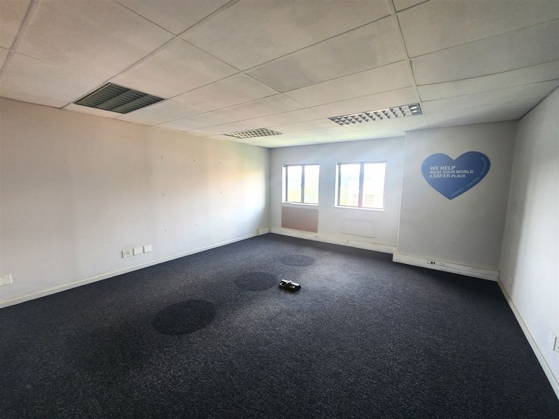 An empty office space featuring a suspended ceiling, recessed lighting, and dark carpet flooring, suitable for a professional workspace setup.
