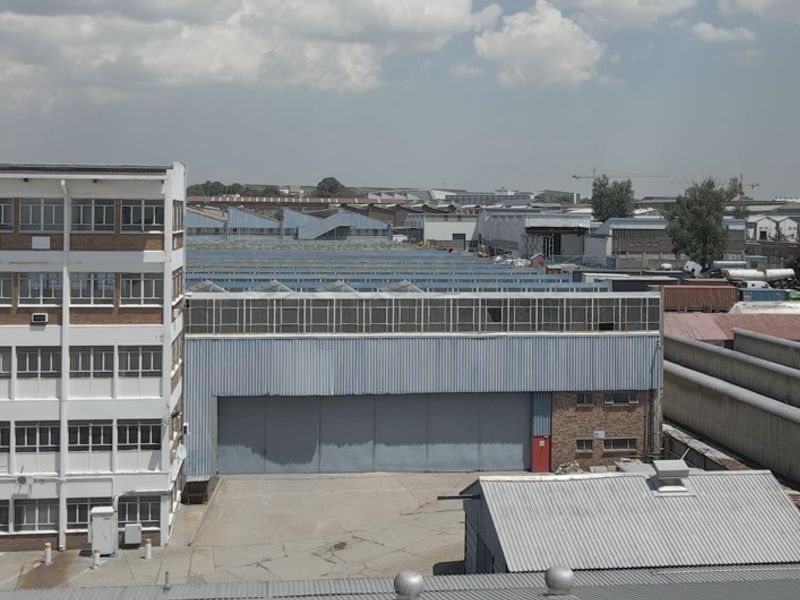 Aerial view of an industrial complex featuring a multi-story office building and adjacent warehouse facility with large roller shutter doors.