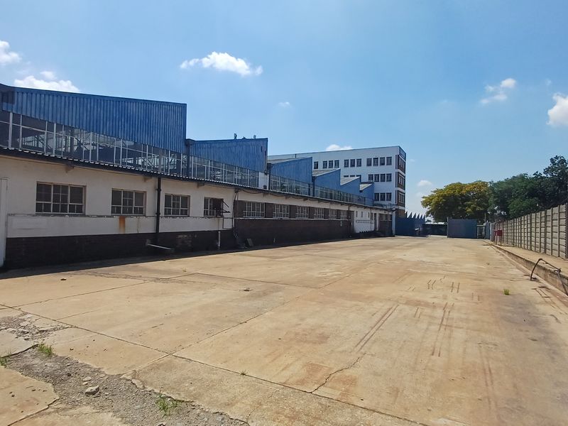 Spacious industrial yard area featuring concrete paving, perimeter walling, and access to the main warehouse structure with sawtooth roof design.