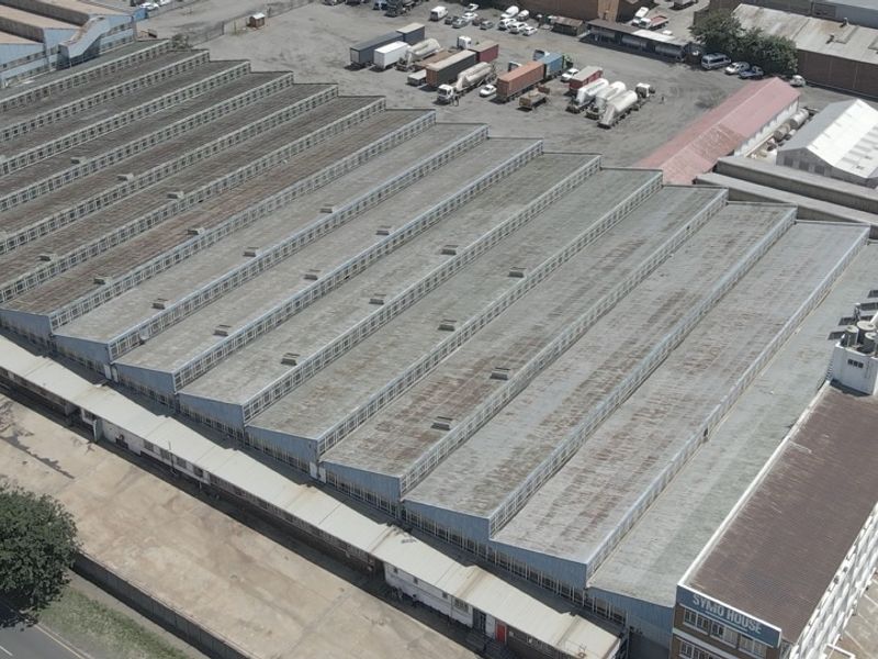 Aerial view of a large industrial warehouse complex featuring a sawtooth roof design, adjacent office building, and paved yard area.