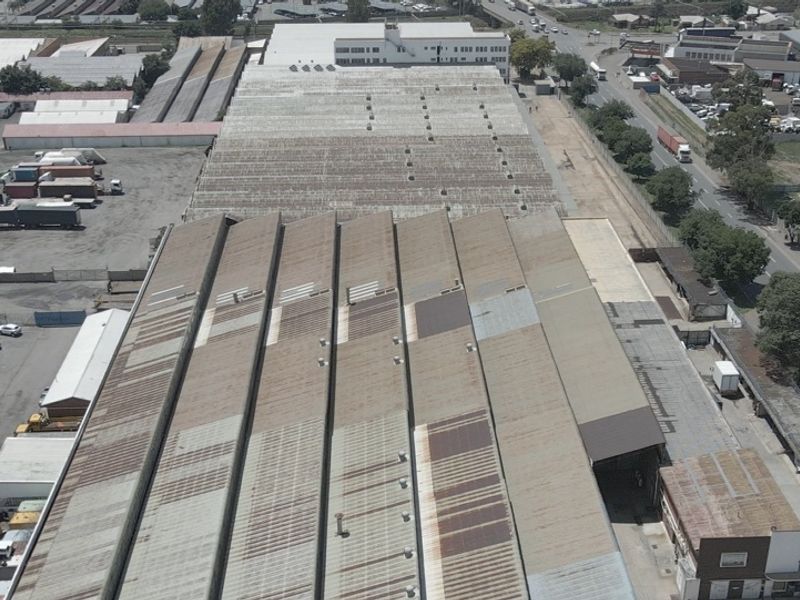 Aerial view of a large industrial facility featuring extensive metal roofing, surrounding yard space, and proximity to major transport routes.