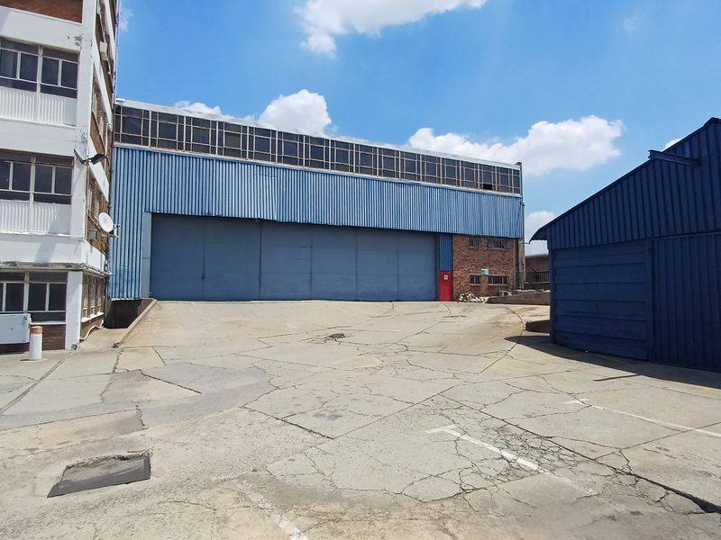 Exterior view of an industrial facility featuring a large warehouse structure with metal cladding, a concrete yard, and adjacent multi-story office building.