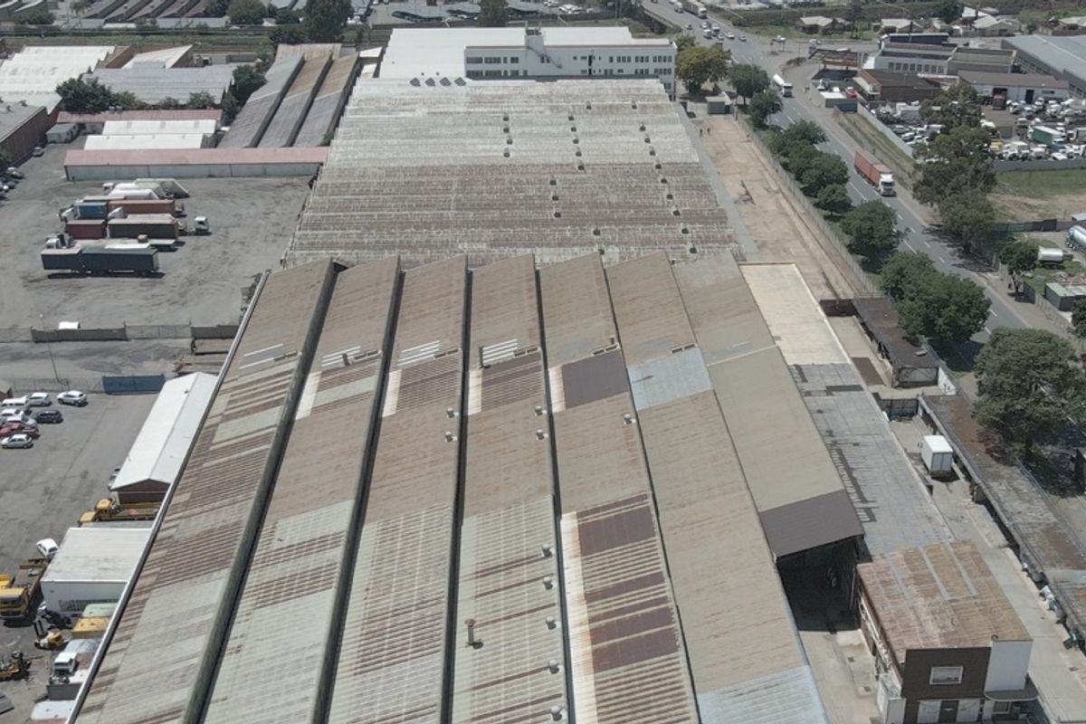Aerial view of a large industrial facility featuring extensive metal roofing, surrounding yard space, and proximity to major transport routes.