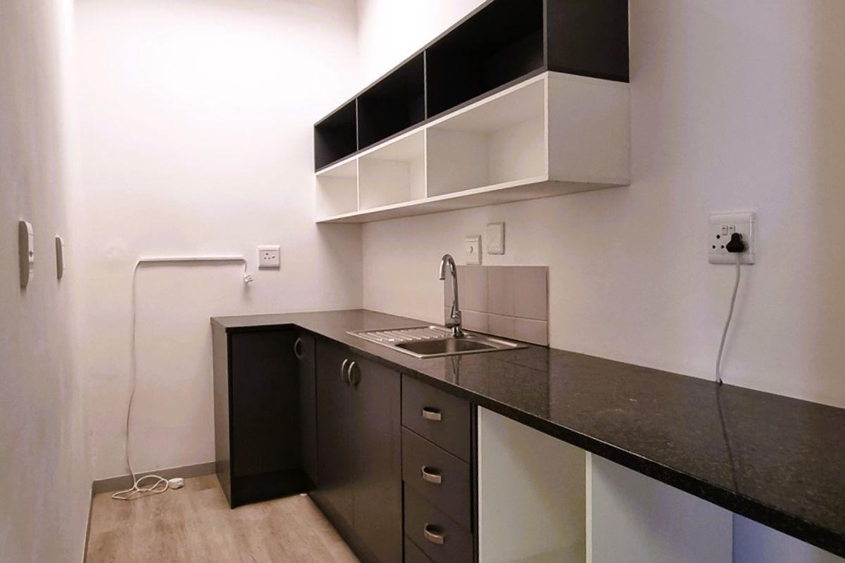 A clean, modern kitchenette featuring dark cabinetry, granite countertops, a stainless steel sink, and ample overhead storage shelving.