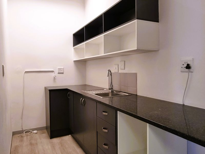A clean, modern kitchenette featuring dark cabinetry, granite countertops, a stainless steel sink, and ample overhead storage shelving.