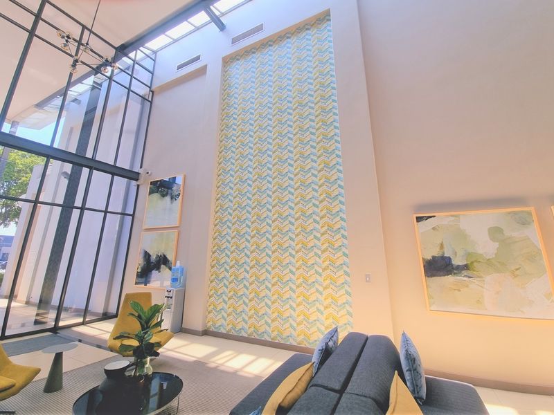 Spacious office reception area featuring a double-height ceiling, large floor-to-ceiling windows, a skylight, and a striking decorative feature wall.
