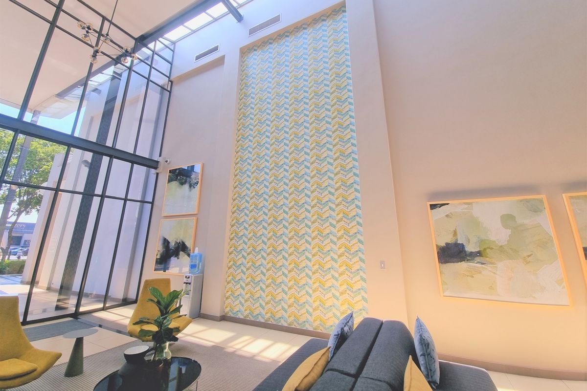 Spacious office reception area featuring a double-height ceiling, large floor-to-ceiling windows, a skylight, and a striking decorative feature wall.