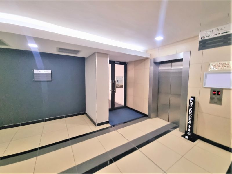 A clean and modern office building hallway featuring tiled flooring, recessed lighting, and a stainless steel elevator.