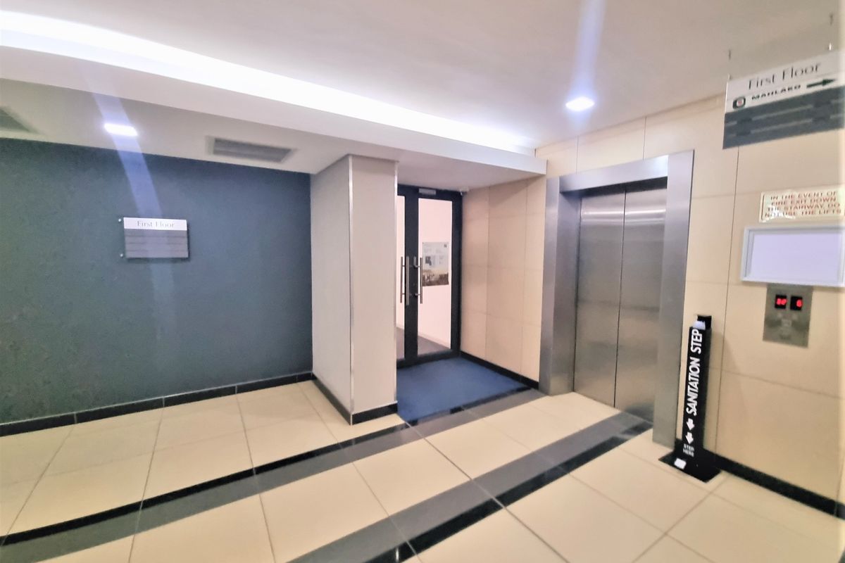 A clean and modern office building hallway featuring tiled flooring, recessed lighting, and a stainless steel elevator.