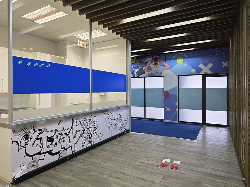 Modern office space featuring a glass partition, built-in cabinetry, and a unique timber slat ceiling design with contemporary flooring.